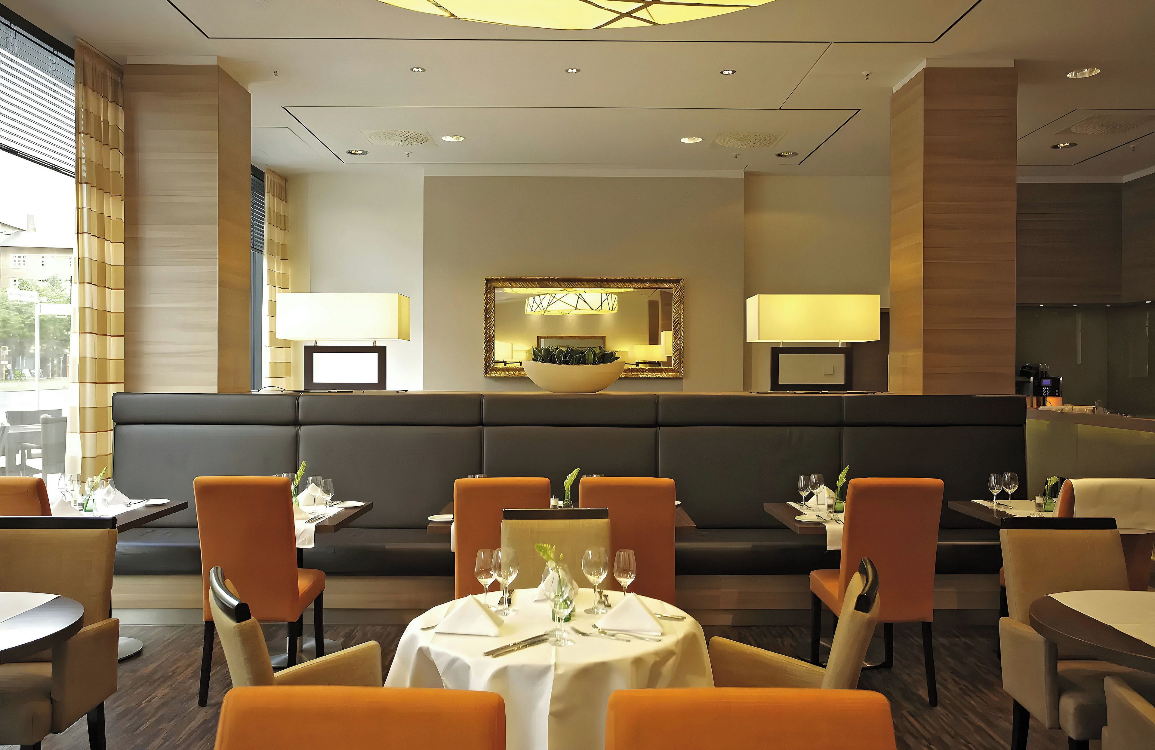 Un restaurante con zona de estar central, mesas individuales y un diseño moderno en el techo.