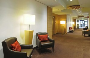 Un vestíbulo de hotel con zonas de estar, lámparas y un pasillo que conduce a una salida.