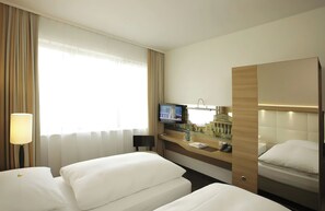 Habitación de hotel con dos camas, televisión, escritorio con teléfono y ventana con cortinas.