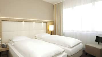 Una habitación de hotel con dos camas, una mesita de noche con lámpara y una ventana con cortinas.