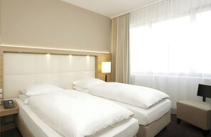 A hotel room with two beds, a bedside table with a lamp, and a window with curtains. - Hotel Berlin Alexanderplatz by Leonardo Hotels (Berlin)