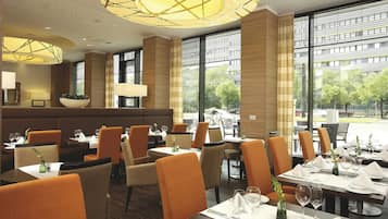 Un restaurante con un interior moderno, que ofrece una variedad de opciones de asientos, incluyendo mesas y cabinas, y amplios ventanales con vistas al exterior.