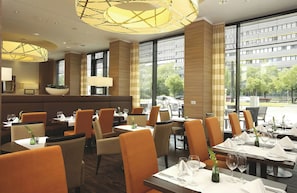 Un restaurante con un interior moderno, que ofrece una variedad de opciones de asientos, incluyendo mesas y cabinas, y amplios ventanales con vistas al exterior.