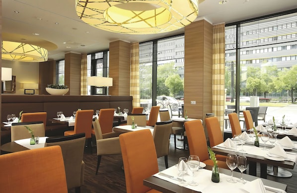 Un restaurante con un interior moderno, que ofrece una variedad de opciones de asientos, incluyendo mesas y cabinas, y amplios ventanales con vistas al exterior.
