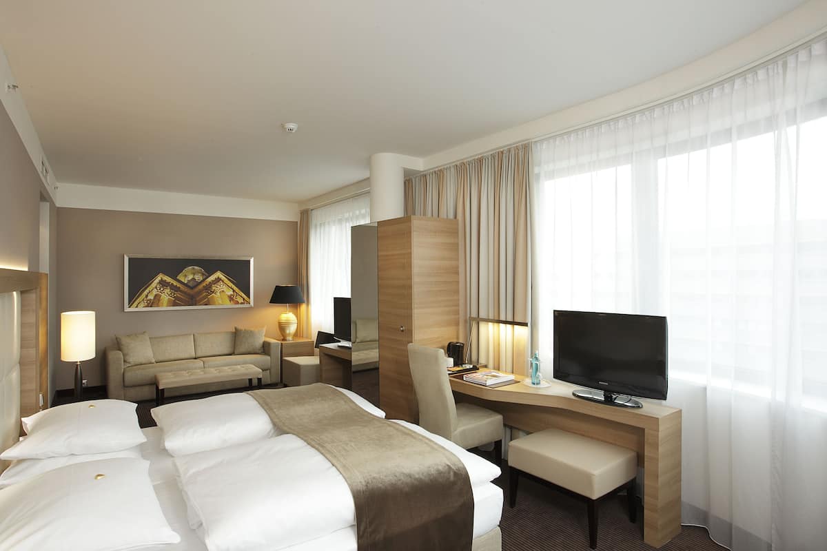 Quarto de hotel com uma cama grande, uma escrivaninha com computador, uma cadeira, televisão e um sofá.