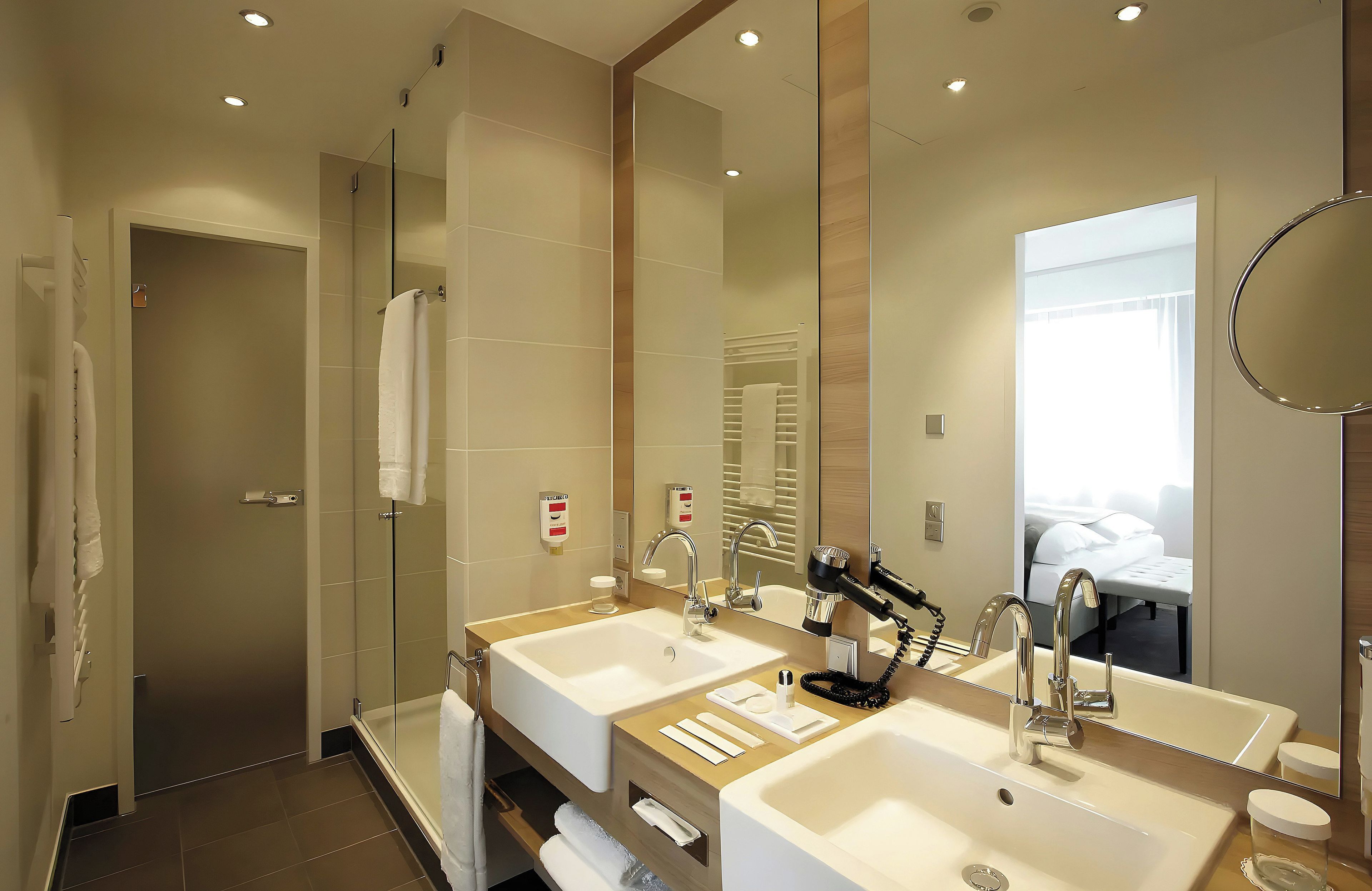 A modern bathroom with two sinks, a shower, and a large mirror.