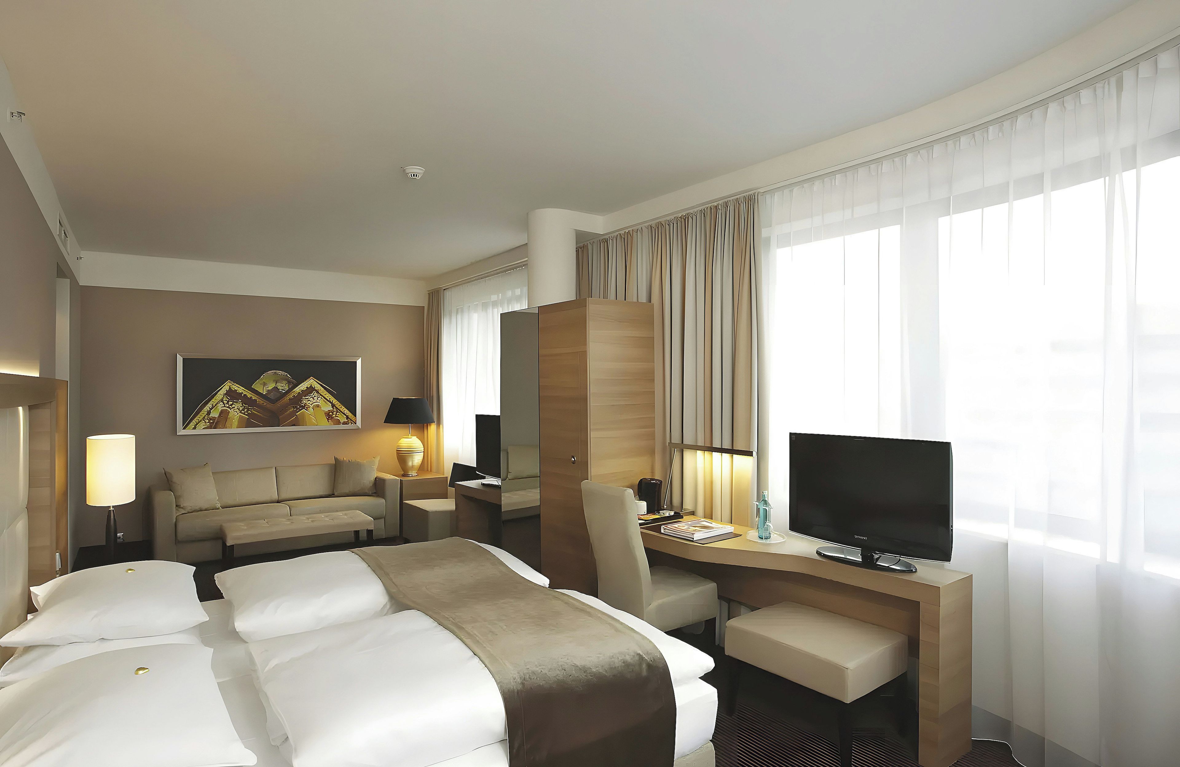 Ein Hotelzimmer mit einem Bett, einem Schreibtisch, einem Stuhl, einem Fernseher und einem Fenster mit Vorhängen.