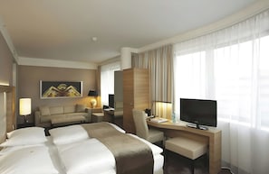 Habitación de hotel con cama, escritorio, silla, televisión y ventana con cortinas.
