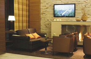 Una sala de estar moderna con un sofá, sillones, una mesa de centro y un televisor de pantalla plana montado en una pared de piedra.