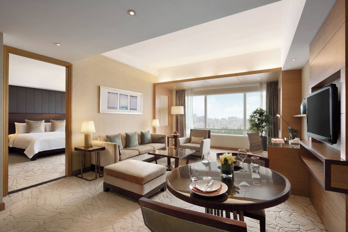 A hotel room with a bed, sofa, dining table, TV, and a city view.