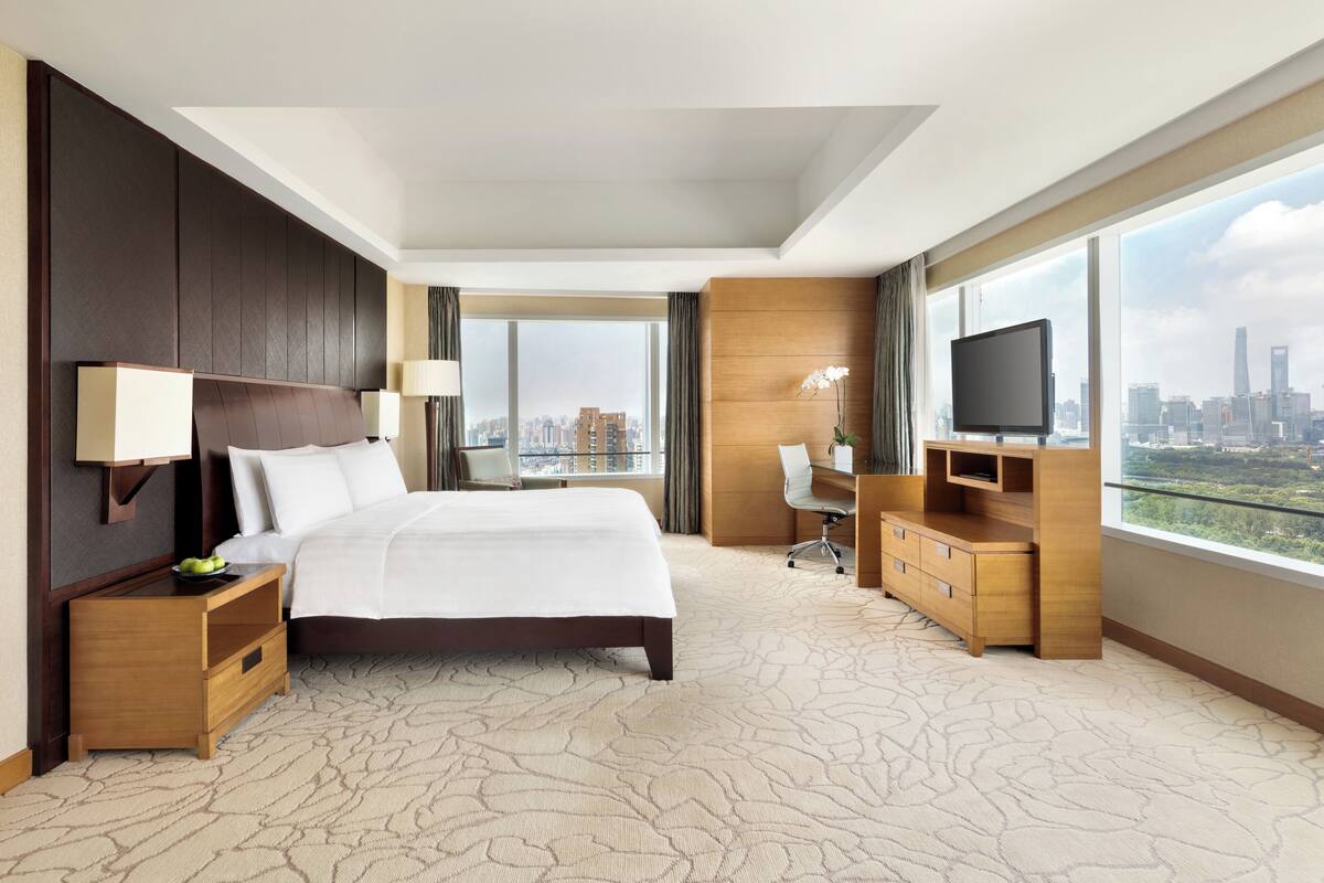 A hotel room with a large bed, a desk, a TV, and a city view.