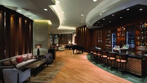 Eine großzügige Lobby mit einem Flügel, einer Bar mit Hockern und einer Sitzecke mit Sofas und Sesseln.