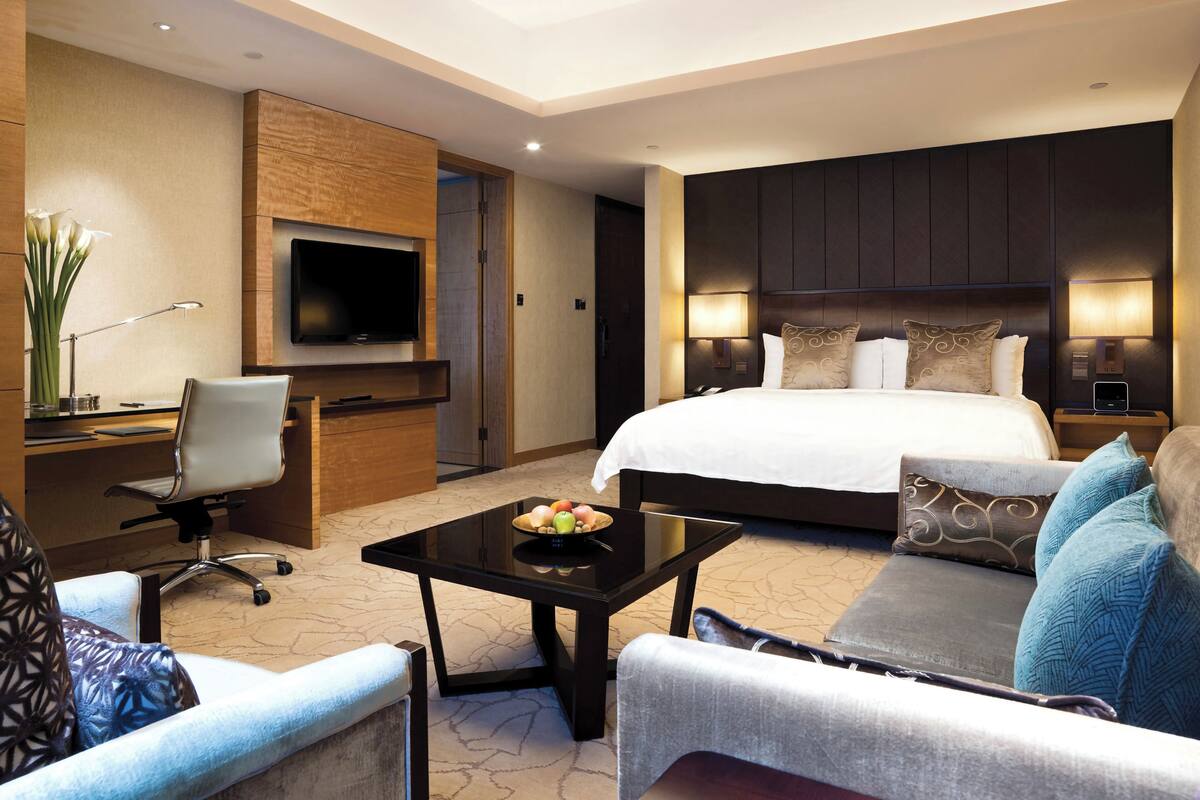 A hotel room with a large bed, a desk with a computer, a TV, and a seating area with a coffee table.