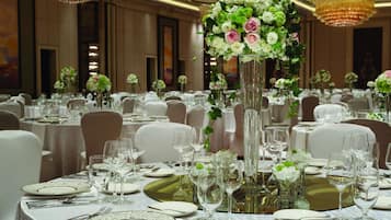 Un salón de banquetes con mesas redondas dispuestas para cenar, cada una con manteles blancos, cristalería y cubertería.