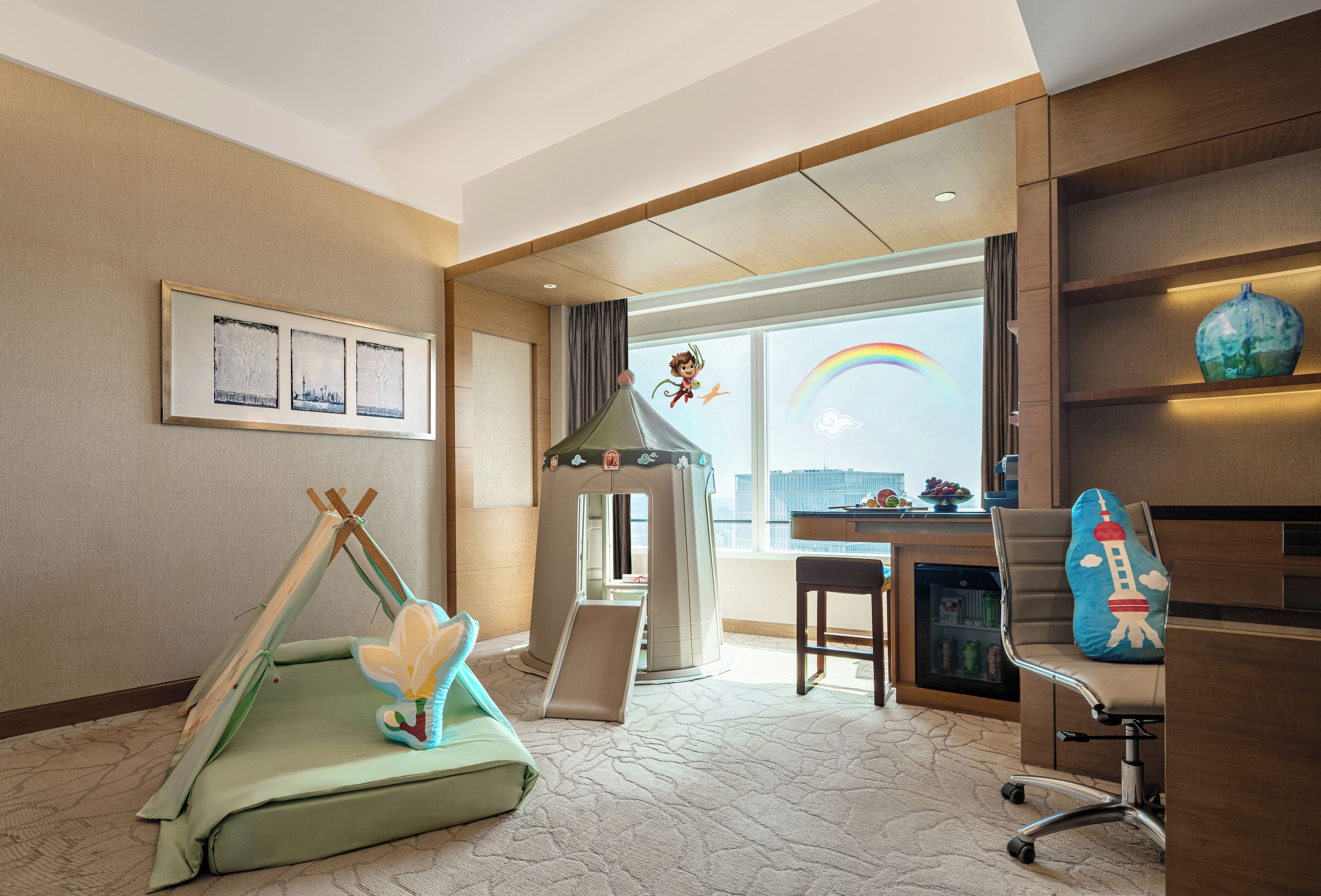 Une chambre d’hôtel dotée d’un espace de jeux, d’un bureau avec un ordinateur et offrant une vue sur le paysage urbain.