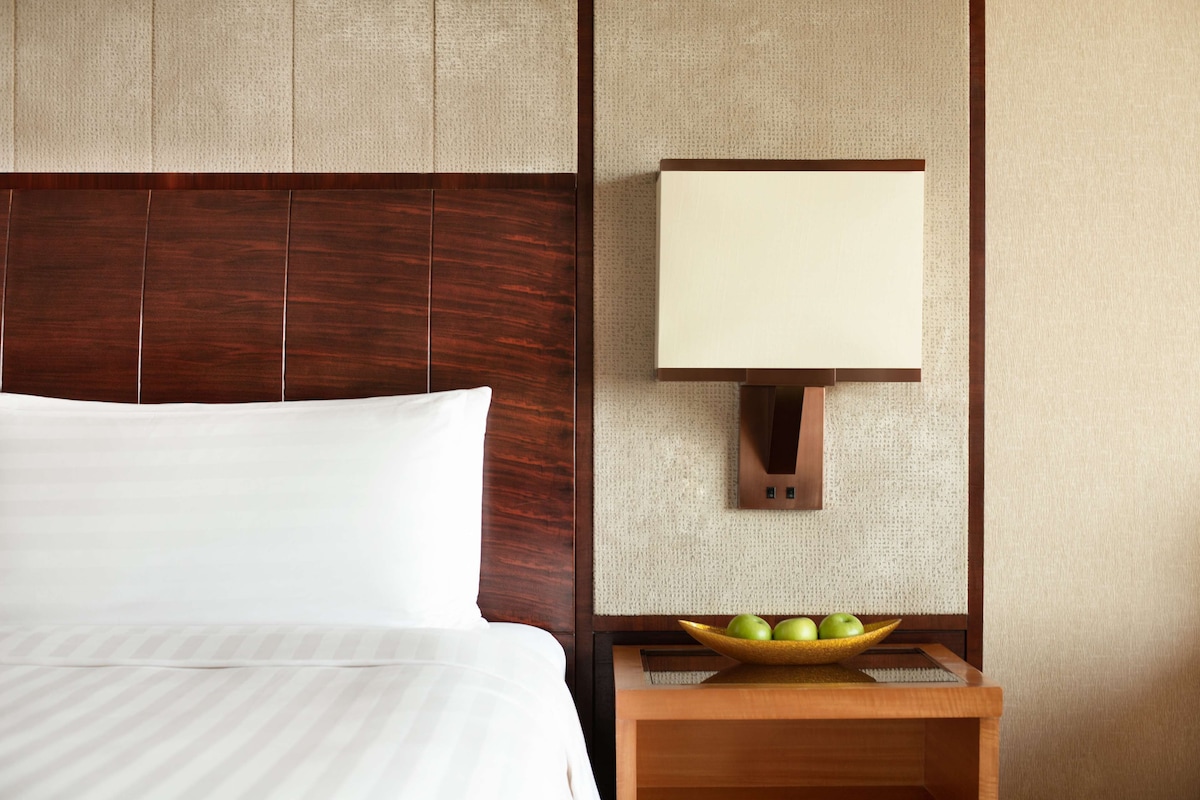 Hotelkamer met een bed, nachtkastje met een fruitschaal en een wandlamp.