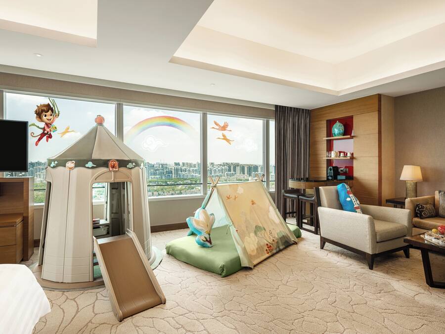 A hotel room with a play tent, a sofa, a TV, and a city view.