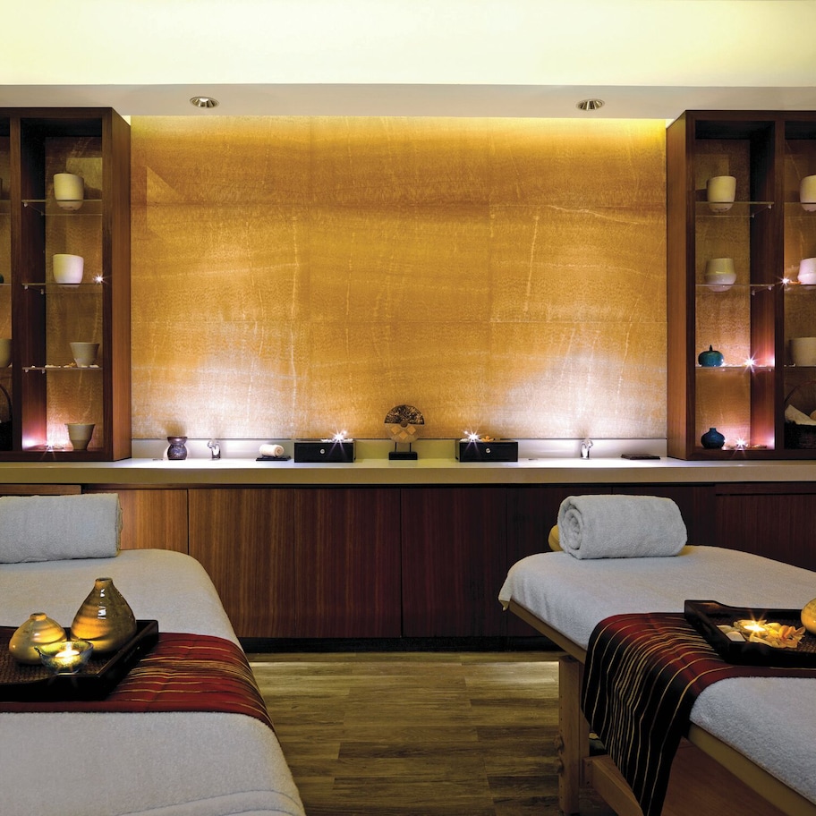 A spa room with two beds, a reception desk, and shelves with candles and small vases.