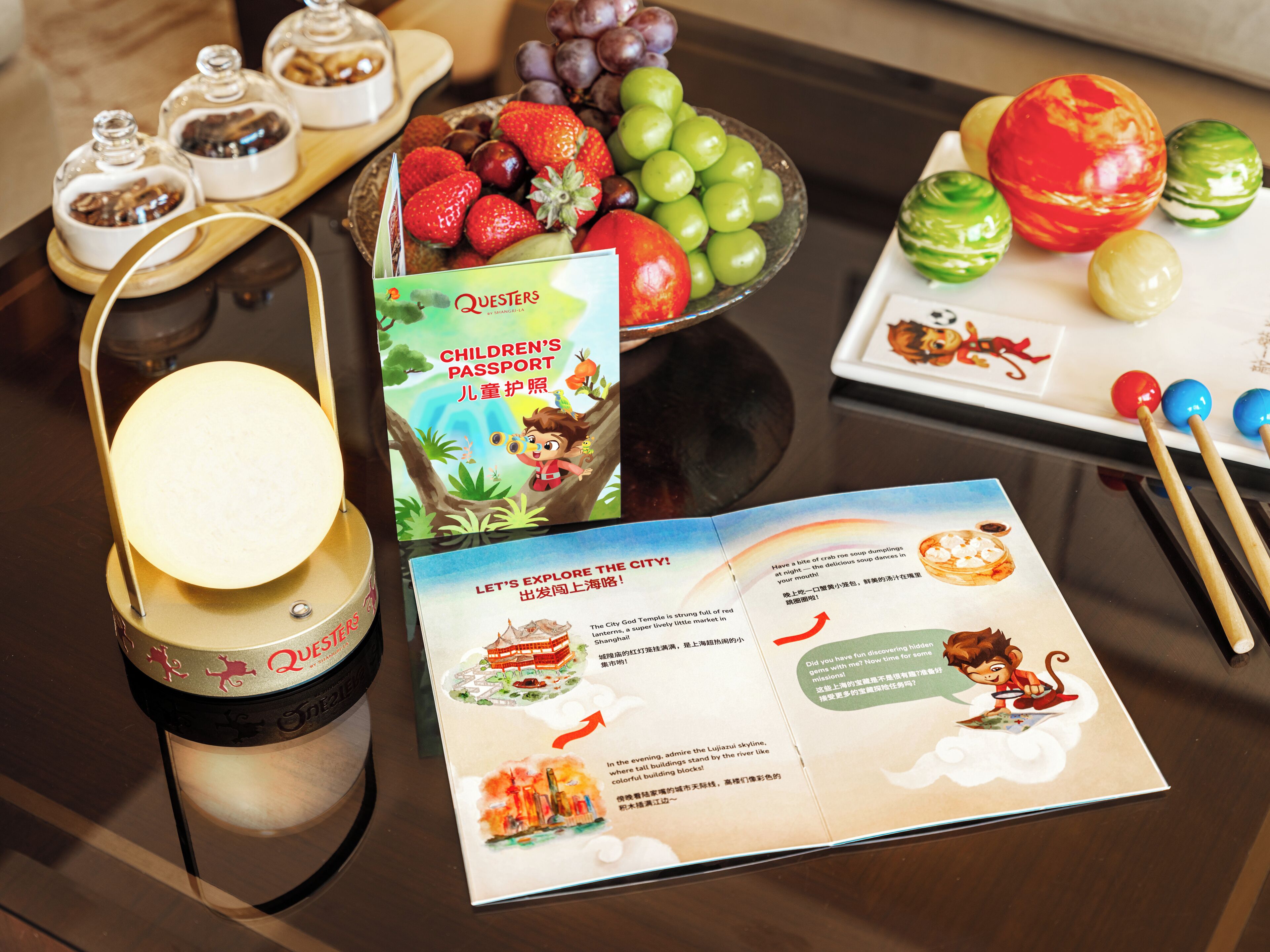 A table with a children's passport, a brochure, a candle, and a fruit bowl.