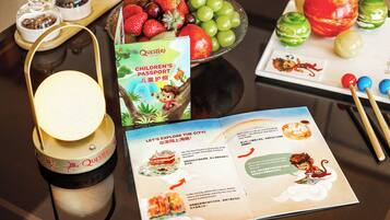 A table with a children's passport, a brochure, a candle, and a fruit bowl.