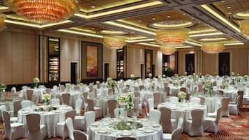 A large banquet hall with round tables set for events, featuring chandeliers and floral centerpieces.