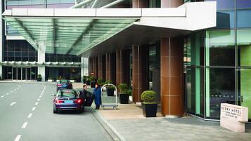 A hotel entrance with a covered walkway, potted plants, and a sign indicating the hotel name.