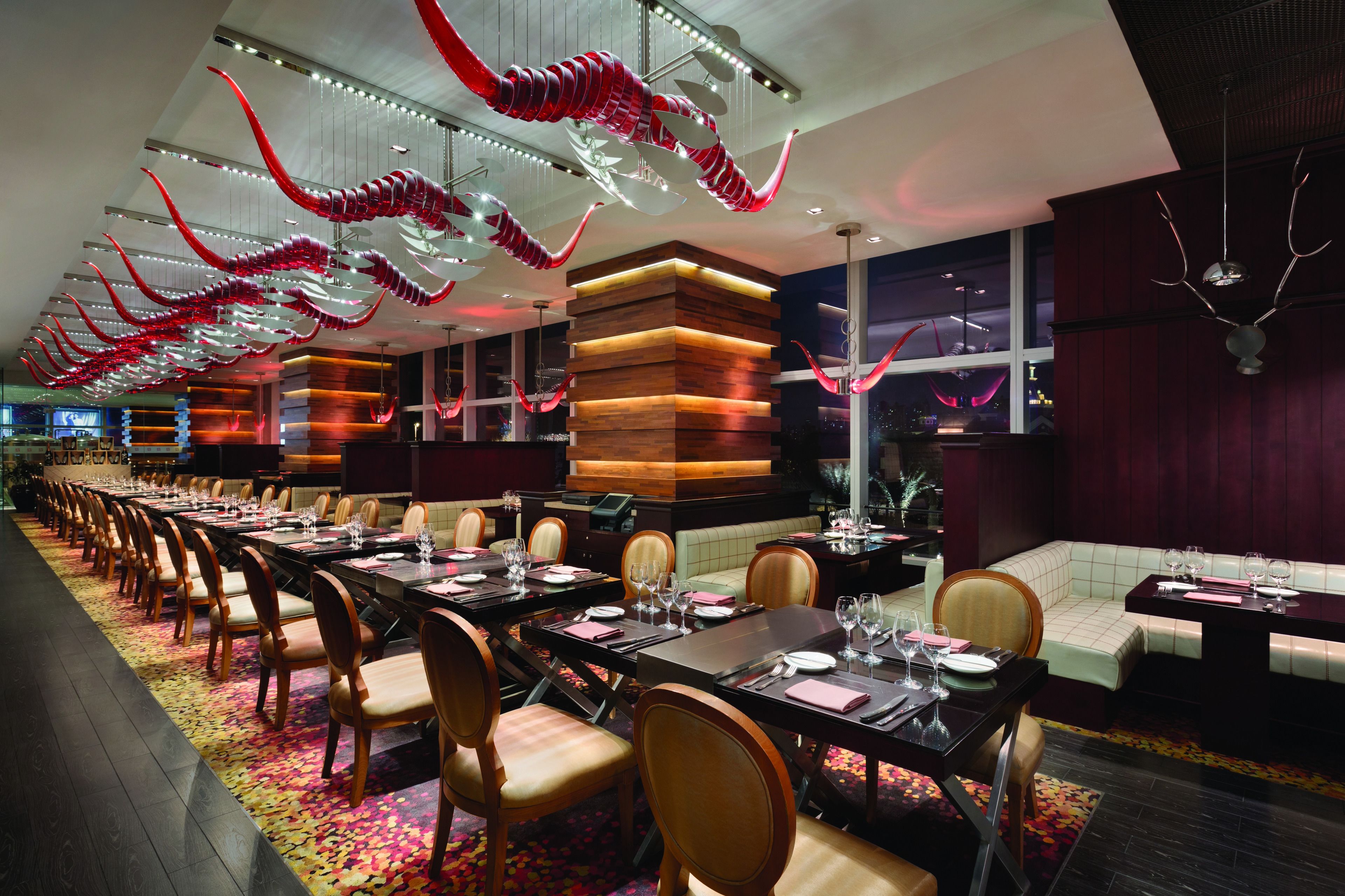 A long dining table with chairs, a wooden accent wall, and a red and white hanging sculpture.