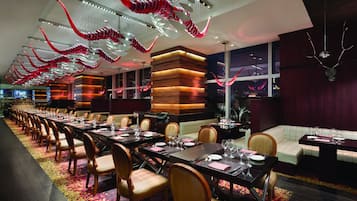 A long dining table with chairs, a wooden accent wall, and a red and white hanging sculpture.