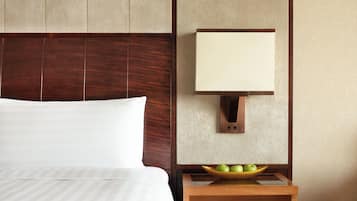 A hotel room with a bed, a nightstand with a bowl of apples, and a wall-mounted lamp.