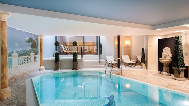 An indoor swimming pool with lounge chairs and a view of a mountain landscape through a glass wall. - Relax Hotel Restaurant Pip Margraff (Sankt-Vith)