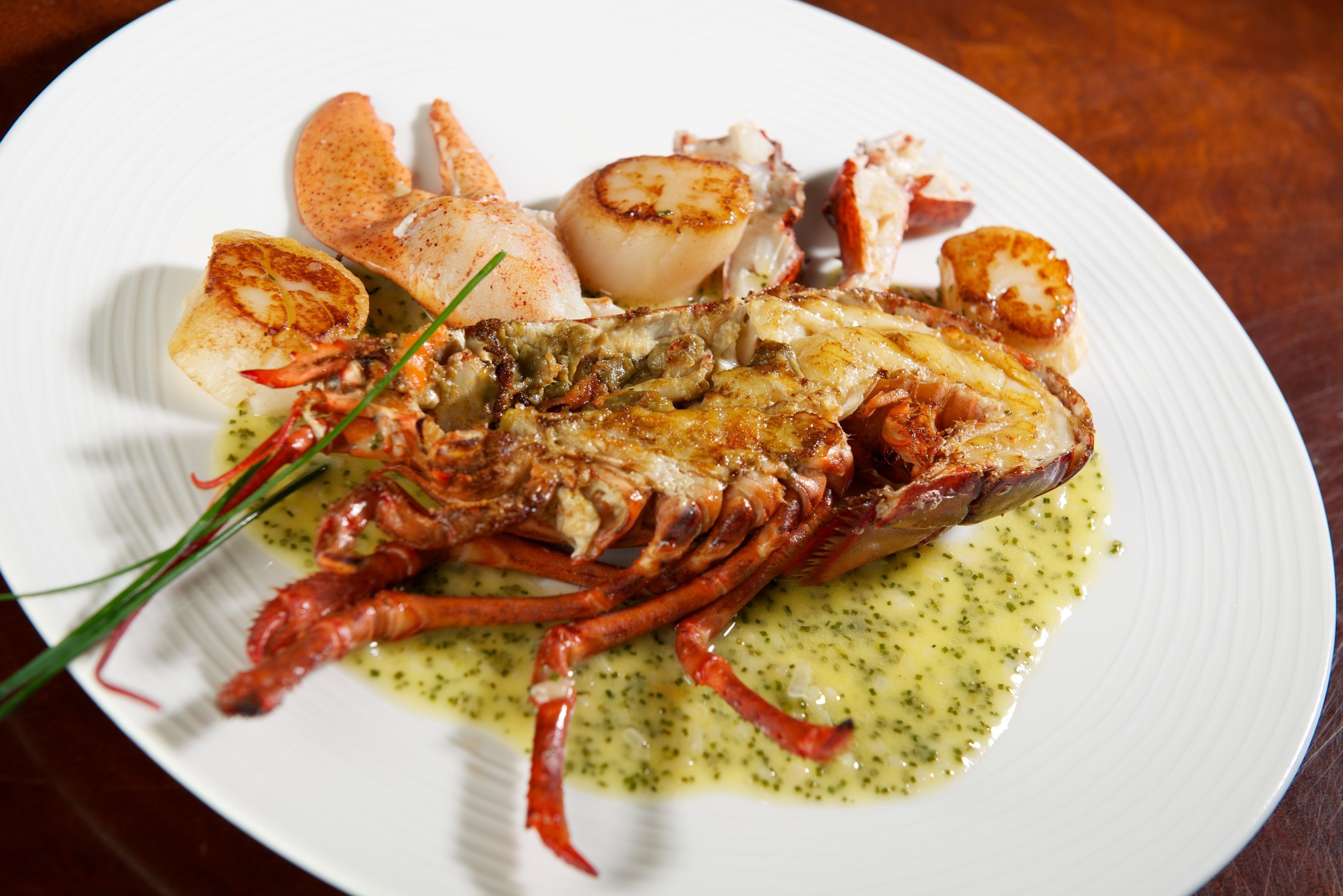A plate of lobster tail, scallops, and a lobster leg with a green sauce.