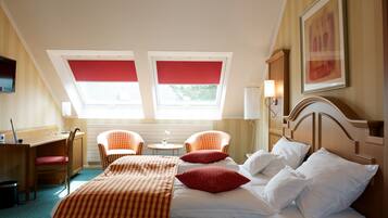 A hotel room with a bed, two chairs, a desk, a lamp, and a painting on the wall.
