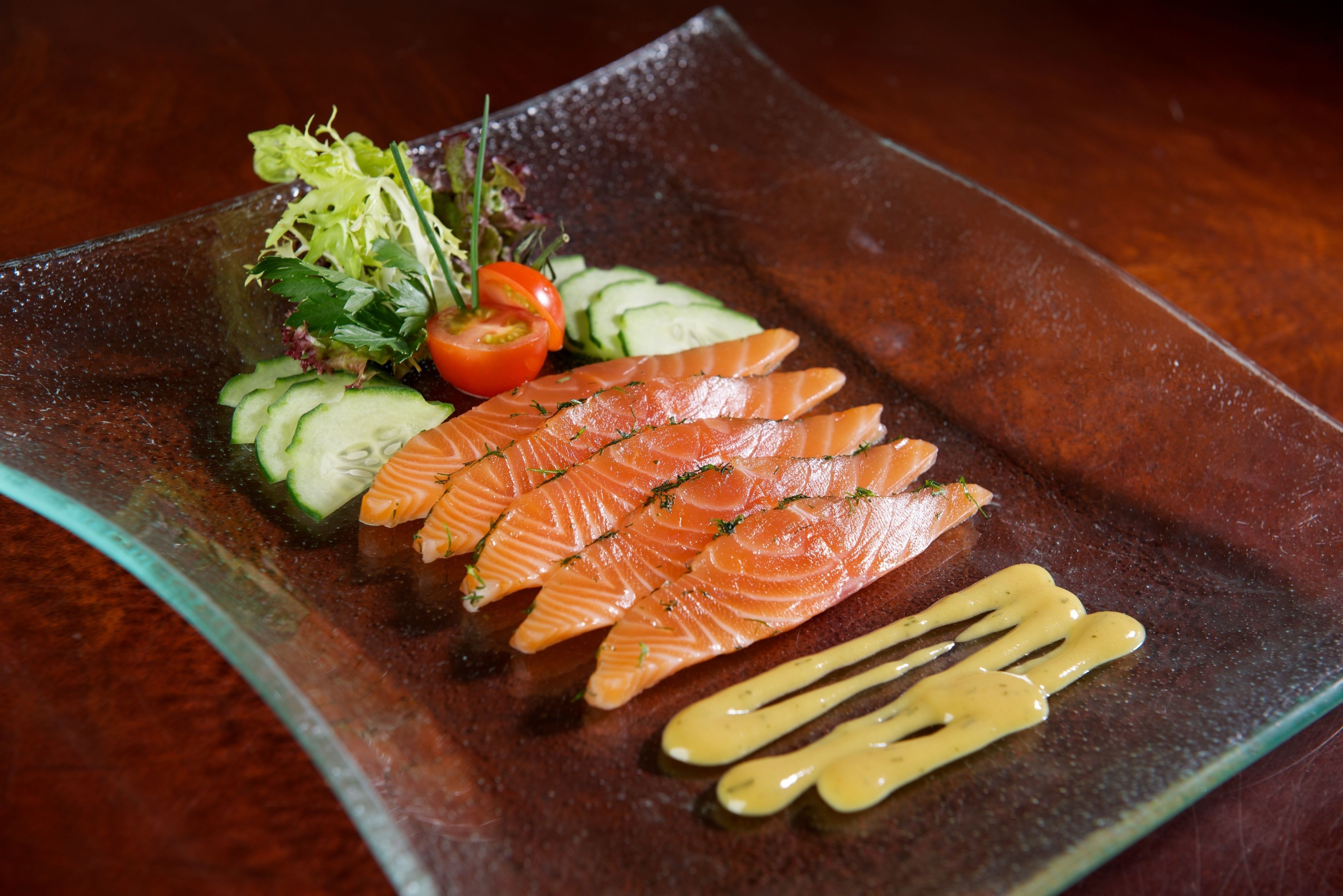 A glass plate with sliced salmon, cucumber, and a small salad.