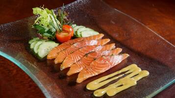 A glass plate with sliced salmon, cucumber, and a small salad.