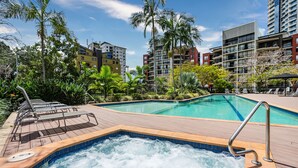 A pool area with a hot tub, lounge chairs, and a view of surrounding buildings.