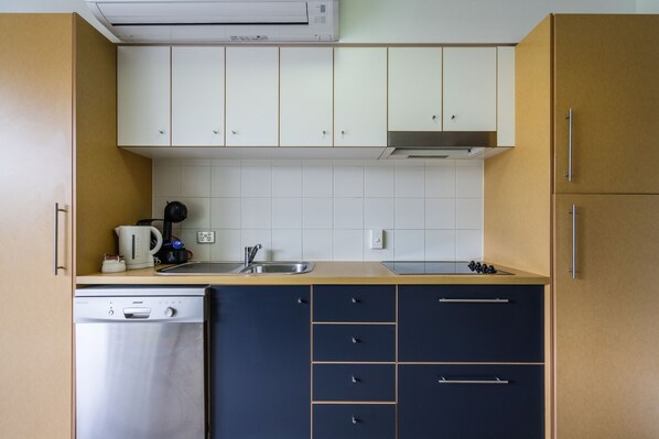 Une cuisine de taille réduite avec des meubles blancs, un lave-vaisselle, une machine à café et une cuisinière.
