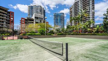 Un court de tennis en plein air, doté d’un filet, entouré de grands immeubles résidentiels et de verdure.