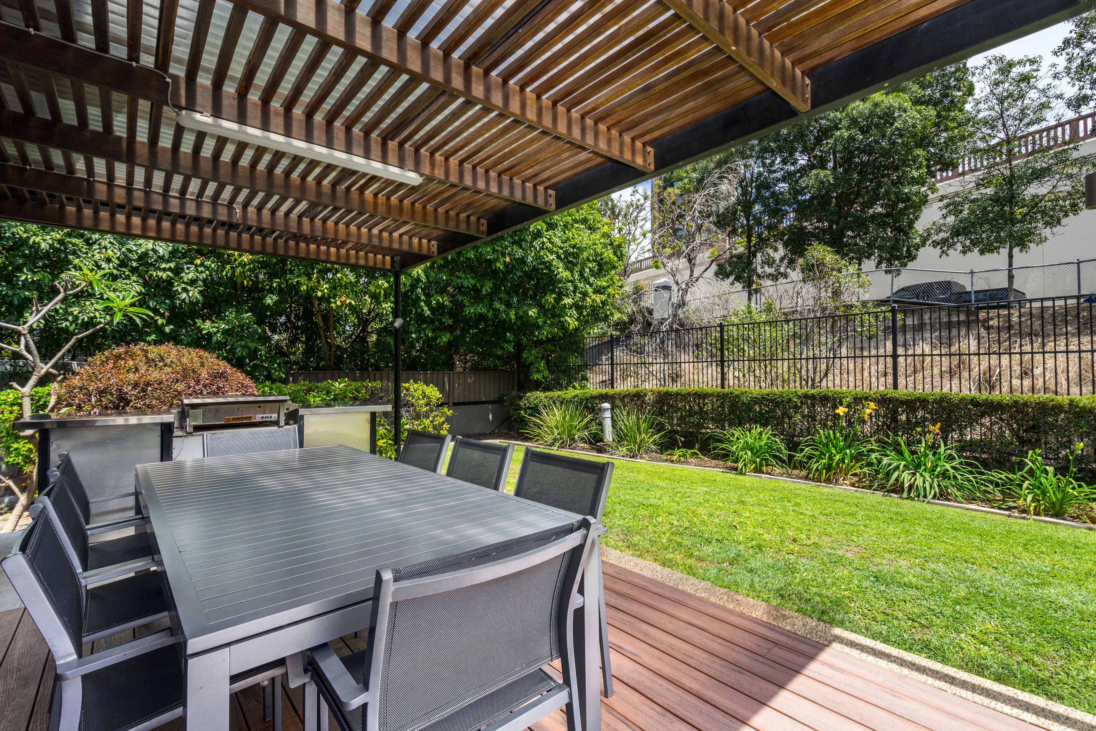 An outdoor patio with a table and chairs, a pergola overhead, and a well-maintained garden.