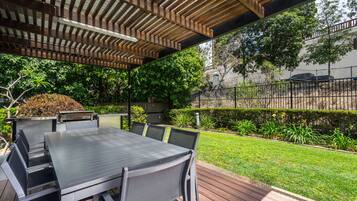 An outdoor patio with a table and chairs, a pergola overhead, and a well-maintained garden.