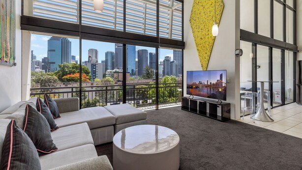 A modern living room with a large window overlooking a cityscape, a sofa set, a coffee table, and a flat-screen TV.