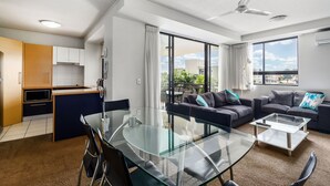 A modern living room with a glass dining table, a sofa, and a balcony with a view.