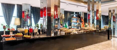 A hotel lobby with a marble reception desk, a buffet area, and a large mirror reflecting the space.