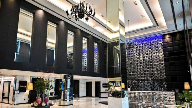 A spacious lobby with a reception desk, a chandelier, and a patterned wall.
