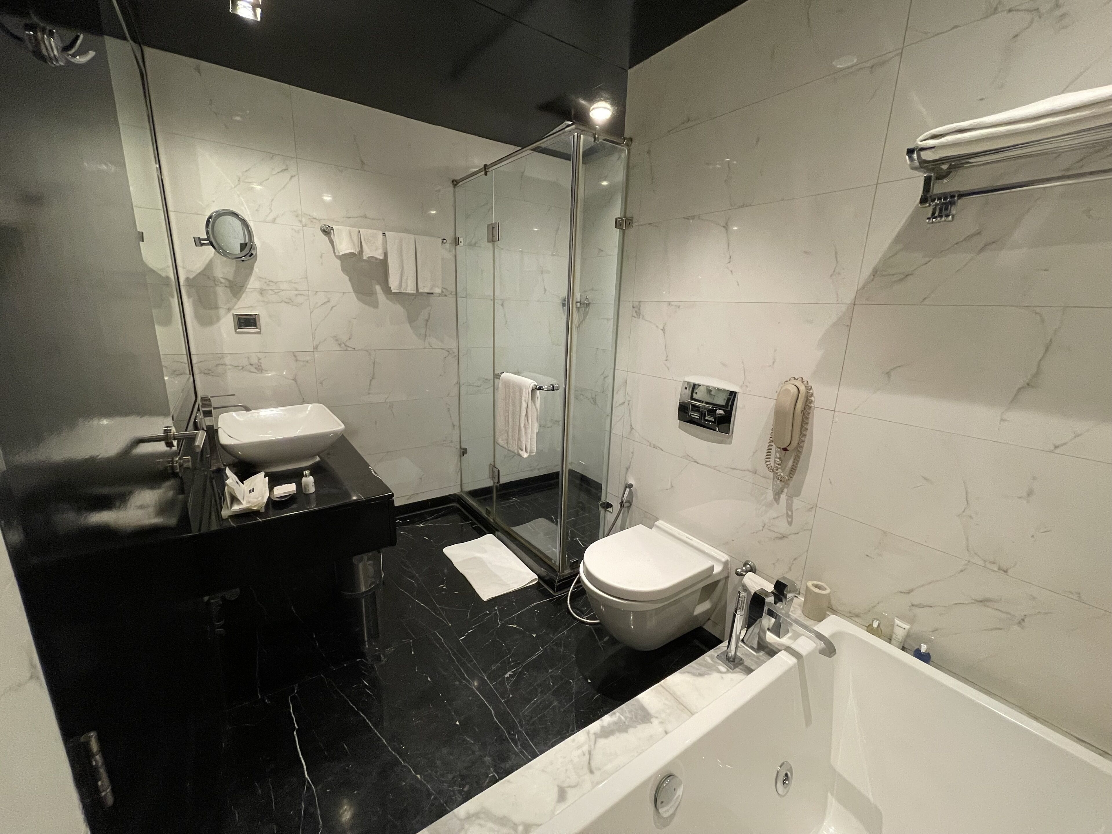 Un baño moderno con cabina de ducha de vidrio, inodoro blanco y encimera de mármol negro.