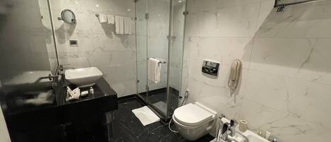 Un baño moderno con cabina de ducha de vidrio, inodoro blanco y encimera de mármol negro.