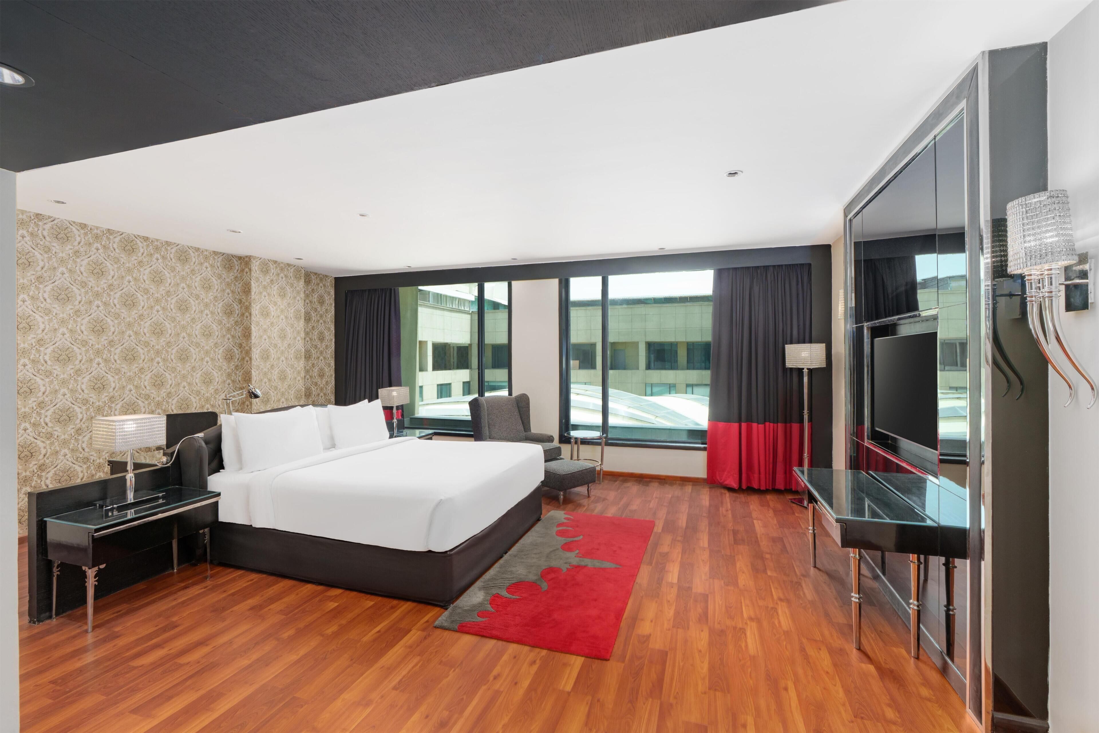 A modern hotel room with a large bed, a desk, a TV, and a view of the outside.