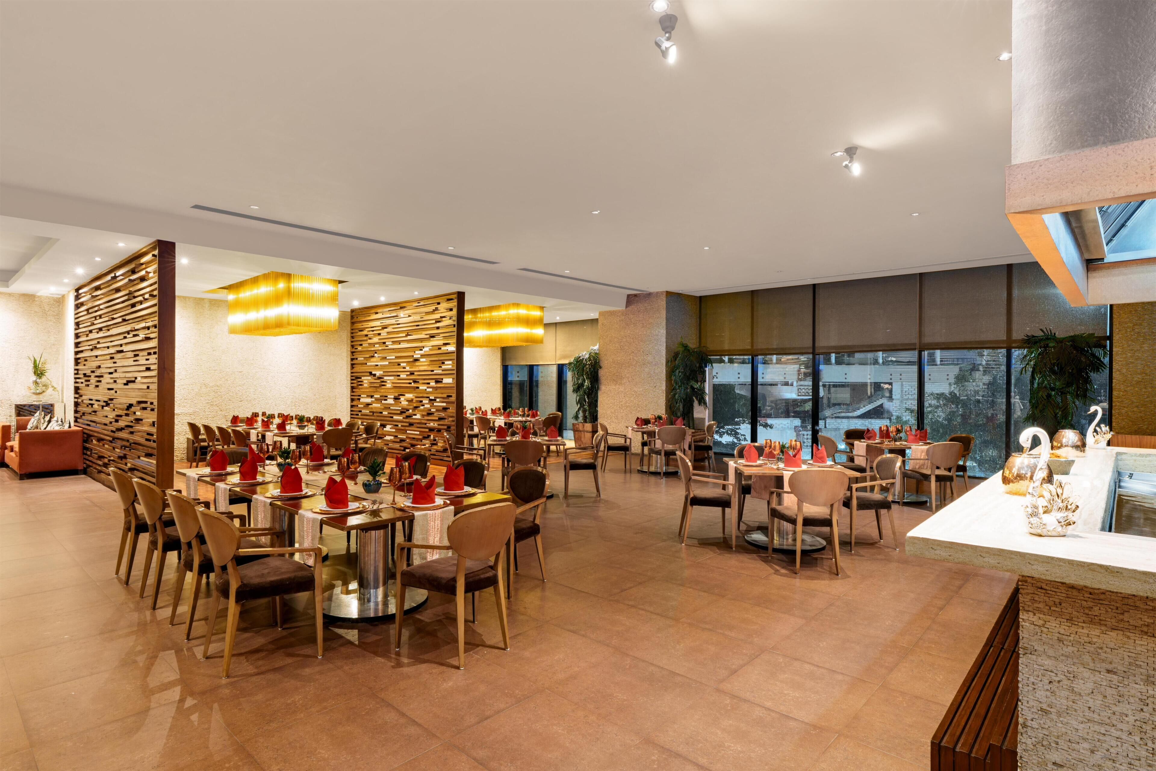 A spacious dining area with multiple tables and chairs, a modern chandelier, and large windows offering a view.