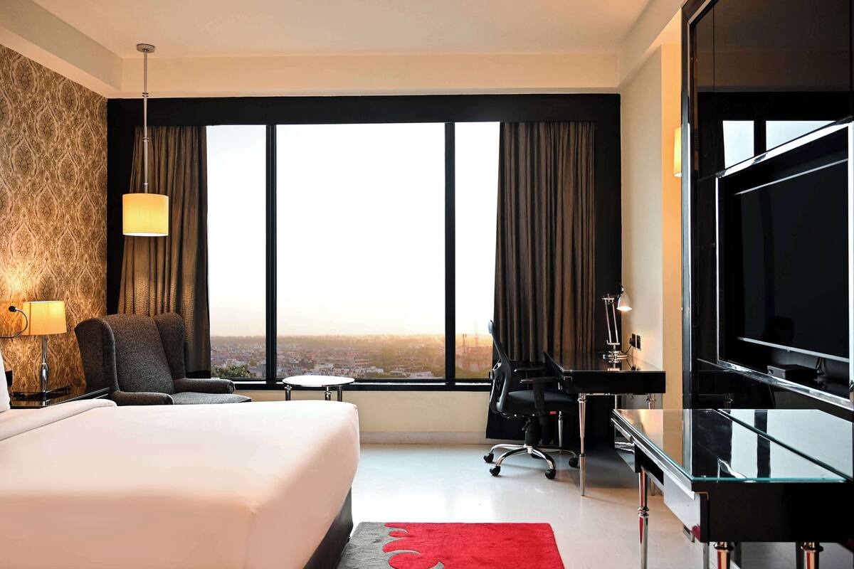 Une chambre d’hôtel dotée d’un grand lit, d’un bureau avec une chaise, d’une télévision et offrant une vue sur la ville grâce à de grandes fenêtres.
