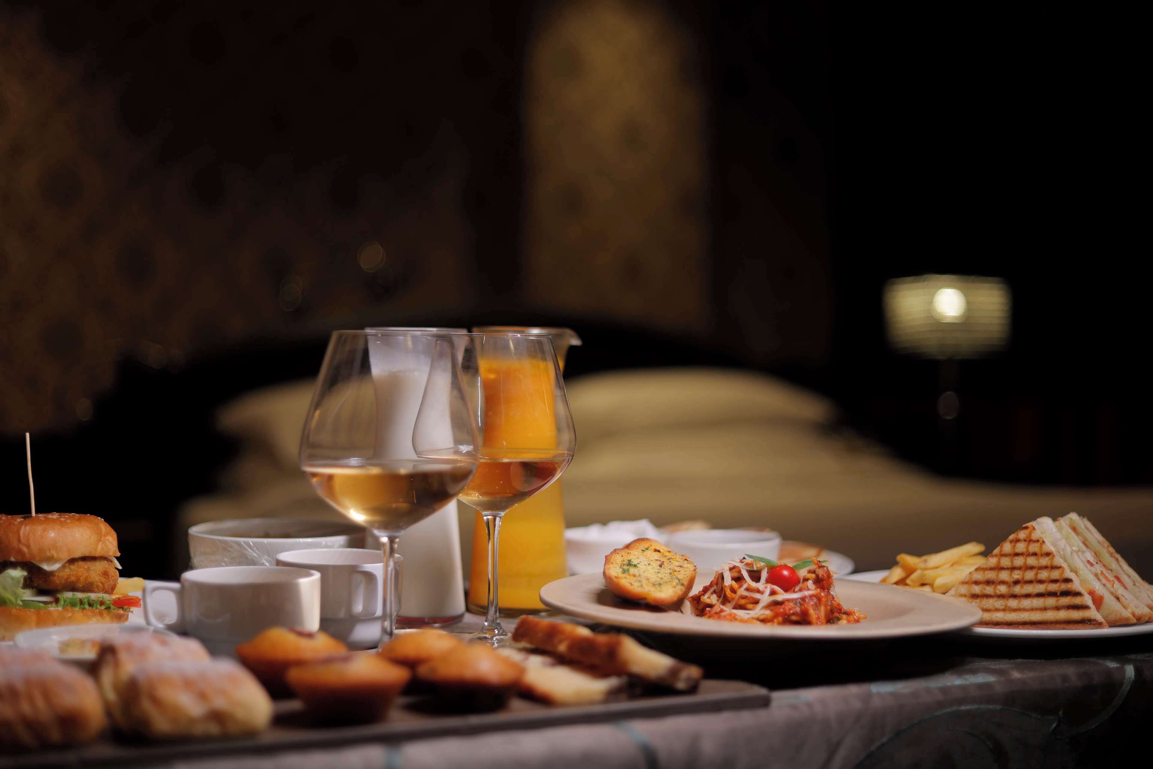 Una mesa de comedor con diversos alimentos, como sándwiches, pasteles y un plato de espaguetis. También hay dos copas de vino y una botella de zumo de naranja.