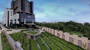 A modern hotel with a prominent 'Radisson' sign, featuring a multi-story structure, landscaped gardens, and a clear sky.